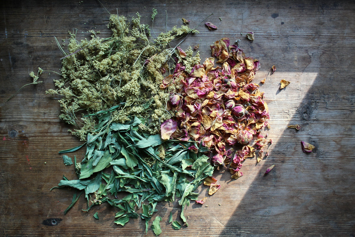 Loose dried herbs and rose petals spread on a wooden surface