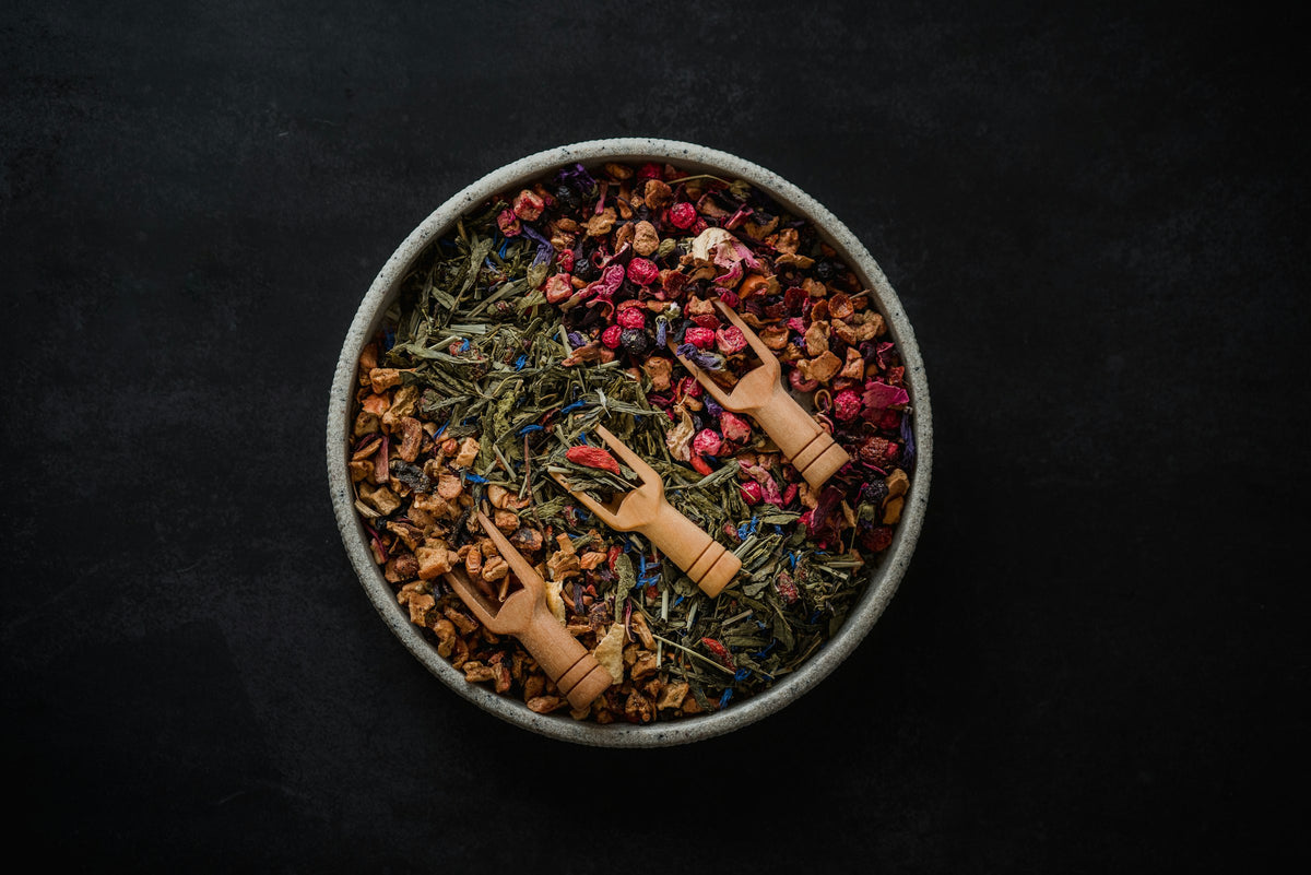 A round tin of dried herbs and flower petals with wooden scoops