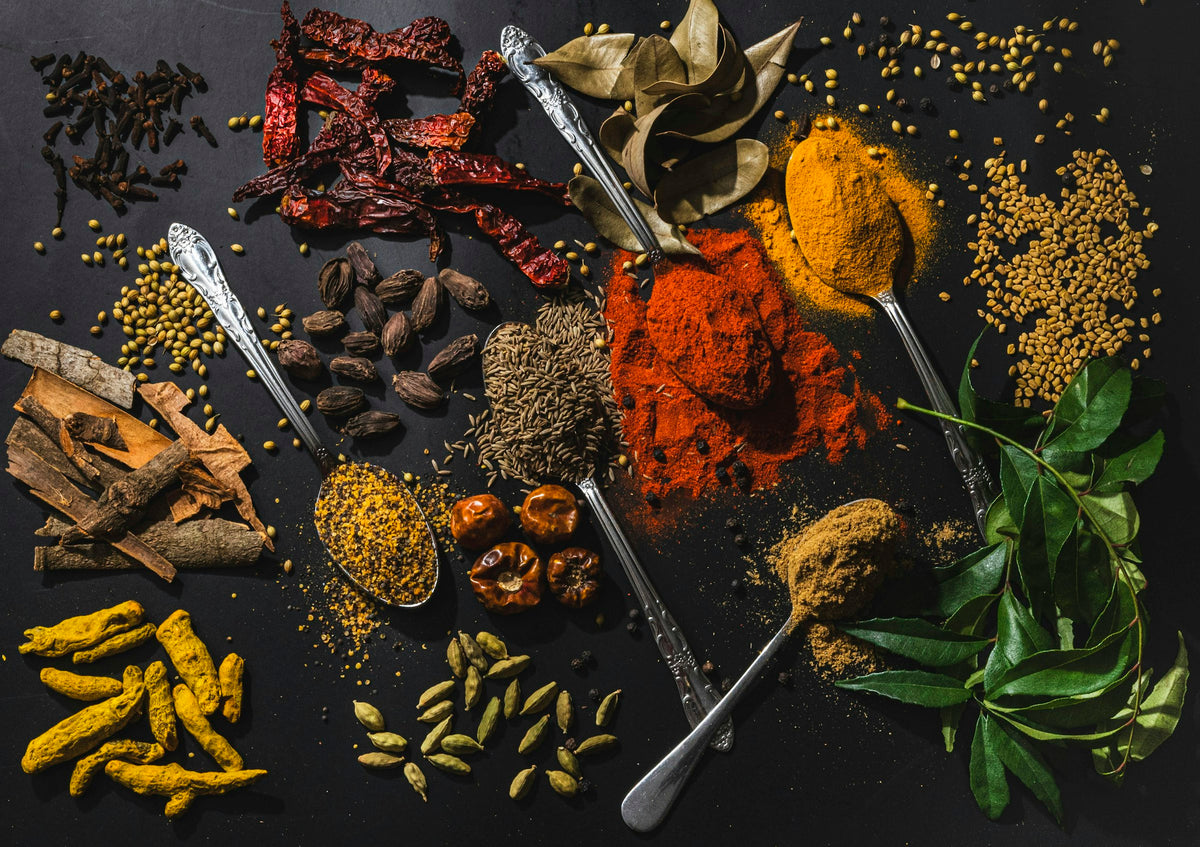 Whole and ground spices with metal spoons on a dark table