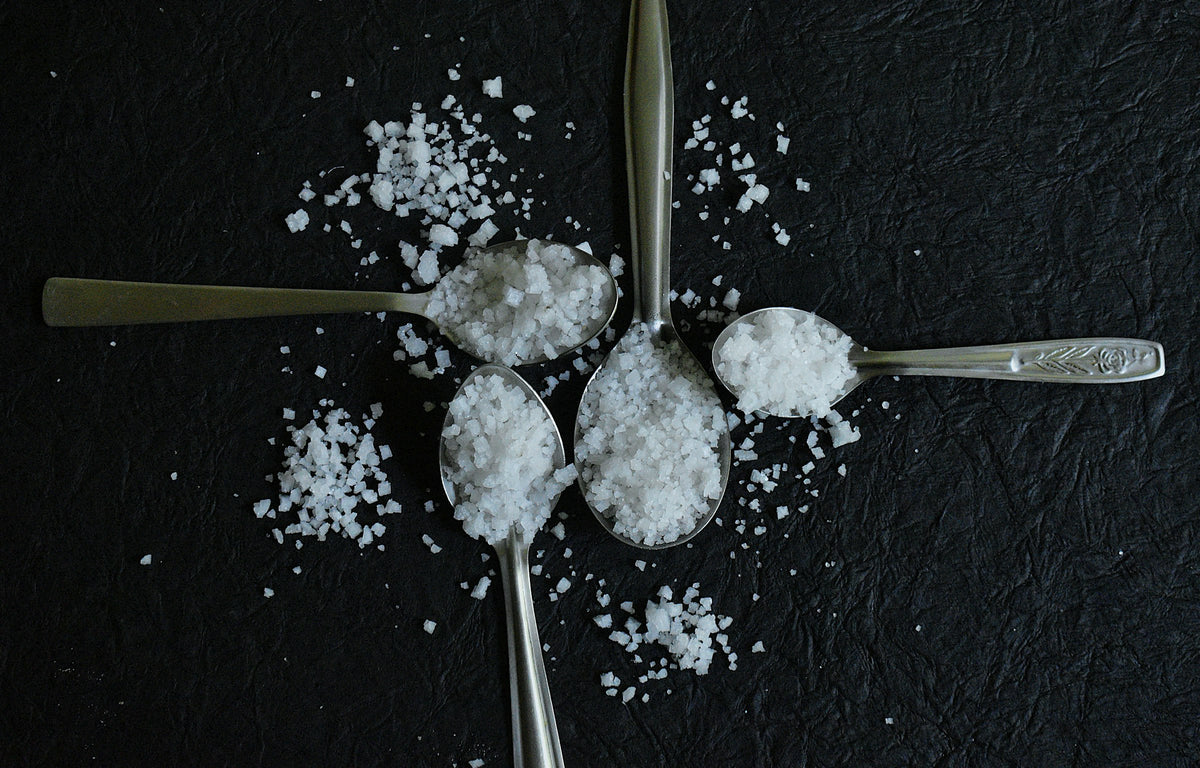 Four spoons of different salts on a dark surface
