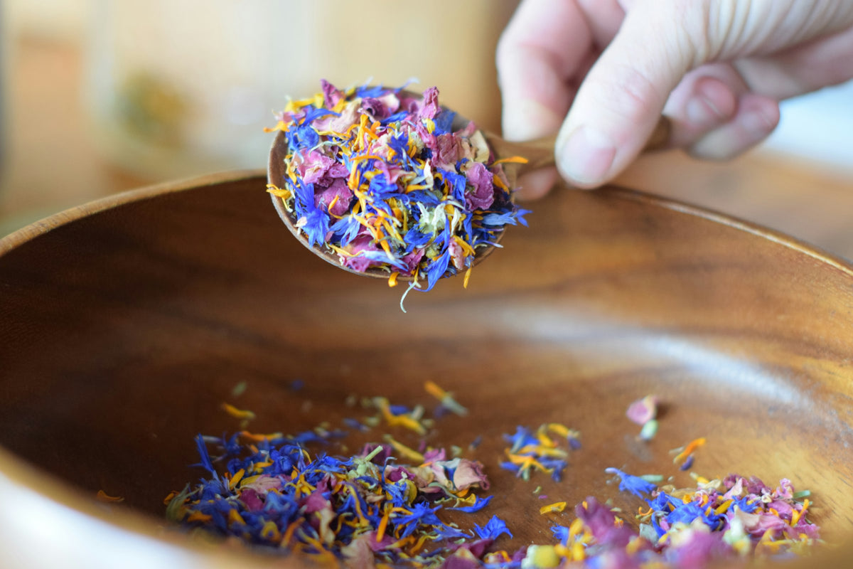 A spoonful of dried flower petals over a wooden bowl